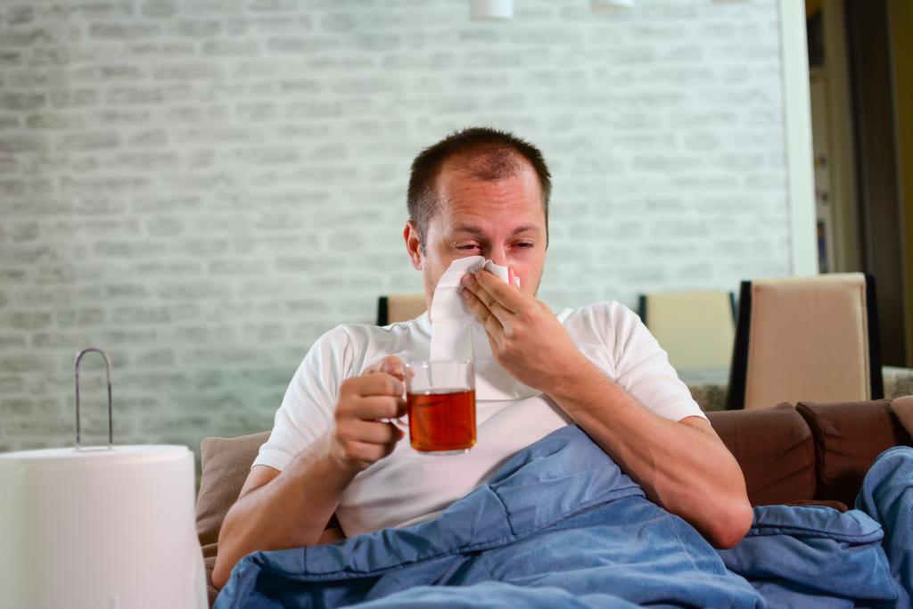 Man zit verkouden op de bank met een glas thee